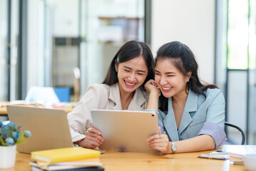 Happy two Asian business woman discuss investment project working and planning strategy on digital tablet. Business people talking together with tablet at office.