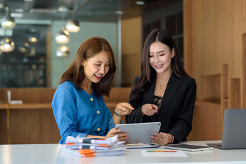 Happy two Asian business woman discuss investment project working and planning strategy on digital...