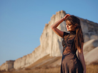 Fashionable woman on desert field near mountain wearing black dress