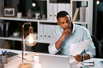 Hes got another bright idea in mind. Shot of a handsome young businessman going over some paperwork while working late in his office.
