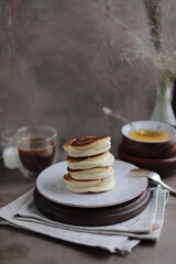 Japanese fluffy pancakes in a plate on the dining table with a cup of coffee and a bowl of honey....