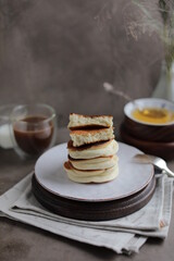 Japanese fluffy pancakes in a plate on the dining table with a cup of coffee and a bowl of honey. Light quick lunch.