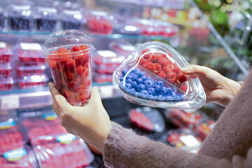 A woman's hand picks fresh berries and raspberries at the supermarket. Wide choice of fresh, organic and healthy products
