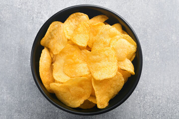 Potato chips. Fast food. Crispy potato chips ceramic black bowl with sour cream sauce and onions in wooden stand on gray kitchen table concrete background. American tradition. Hot BBQ. Top view.