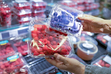 A woman's hand picks fresh berries and raspberries at the supermarket. Wide choice of fresh, organic and healthy products