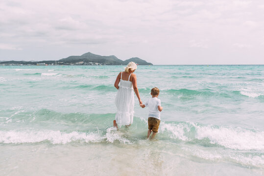 Mama und Kind mit weißen Kleid am Strand im wasser und Wellen spielend auf Mallorca