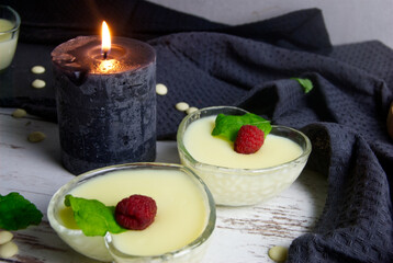 Pudding dessert with raspberry and mint on wooden floor. Near the candle.