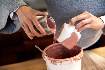 Ceramic Artist putting finish ceramic glaze on a crafted cup in her studio workshop
