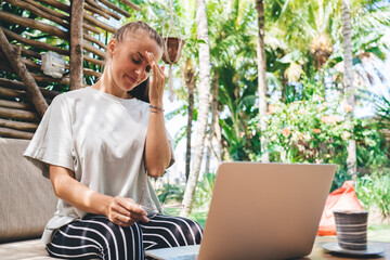 Tired female with laptop computer feeling tired during overtime remote working at terrace,...