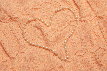 Valentine's Day image with white perl necklace in heart shape on a coral color lace background