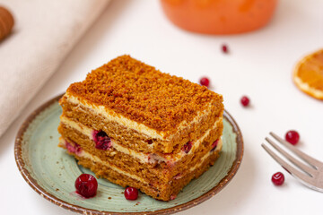 Close up of a tasty cake with cream and red berries on the plate, a bright orange creamer, ceramic cup, fork on white table, delicious dessert concept