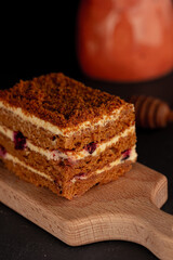 Close up of a tasty cake with cream and red berries on wooden plate on black