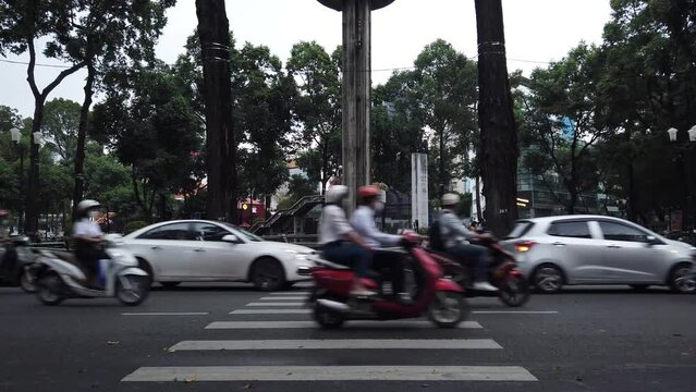 motorbike and car traffic in central Saigon district one with turtle lake in the background. Forground features a pedestrian crossing.