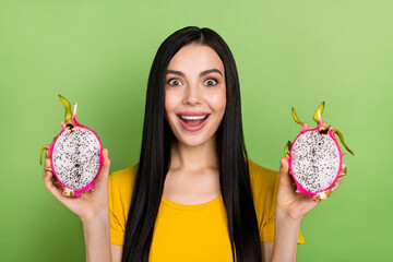 Portrait of cheerful person hold two halves dragonfruit toothy smile look camera isolated on green...