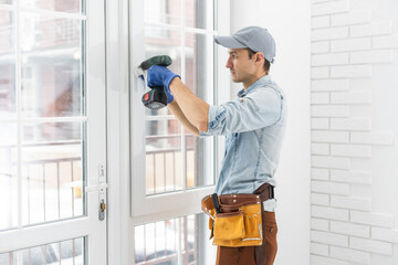 handyman adjusting white pvc plastic window indoors. worker using screwdriver to repair upvc window. homework maintenance.