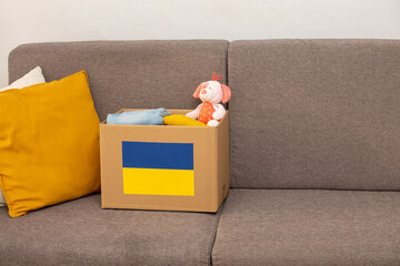 Close up box with Ukrainian flag for humanitarian aid donation with children's things and toys at...