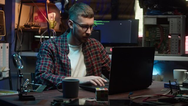 Hacker using laptop. Young man developing program in dark room. Professional programmer infecting system with cyber virus, typing on computer keyboard, breaking password.