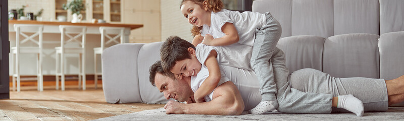 Low angle of jolly son and daughter on dad back while he is lying on floor during training at home