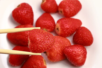 A strawberry close-up with chopsticks, other strawberries in the background