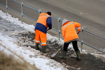 Two workers with shovels cleaning sidewalk, snow and melting ice removal in spring city