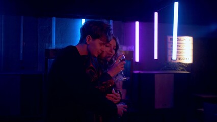 A sensual couple flirting, dancing, kissing under neon lights in a nightclub. The couple drinks alcohol, dances and kisses. Night club