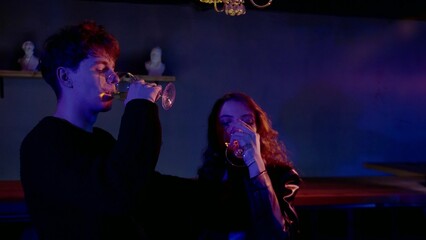 A sensual couple flirting, dancing, kissing under neon lights in a nightclub. The couple drinks alcohol, dances and kisses. Night club