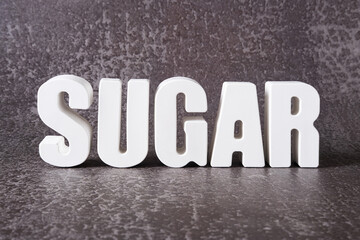 Fototapeta na wymiar Word Sugar made from white concrete letters on the gray background