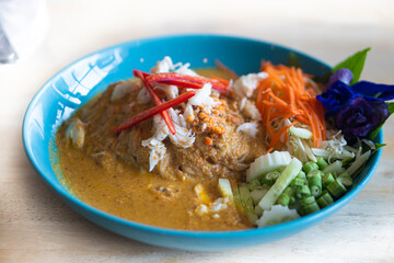 Rice noodles in crab curry sauce with vegetables arranged in a blue dish.
