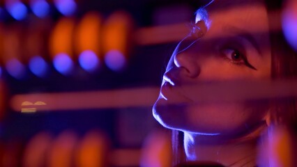 Close-up of a girl counting on old wooden accounts under neon light. Night club. Beautiful compositions with people in neon light. A model girl poses for the camera under a neon light.