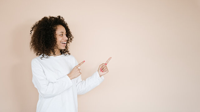 Portrait of smiling young african american woman giving information, showing way, pointing fingers right at copy space aside, standing upbeat against brown background
