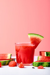 Fresh watermelon juice or smoothie in glasses with watermelon pieces on pink background. Refreshing summer drink