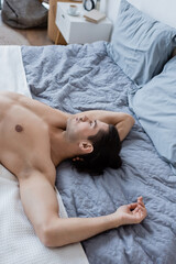 top view of shirtless man with long hair lying on bed at home.