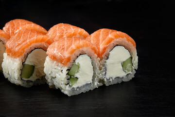 Philadelphia roll sushi with salmon, cucumber and cream cheese on black background for menu. Japanese food