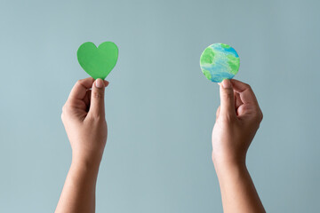 Hands holding earth and green heart shape. Concept of protecting the world from global warming with eco-heart in mind.