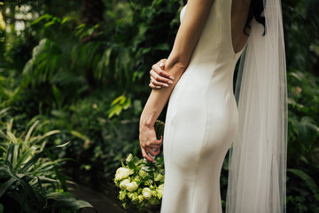 Young bride in a elegant sexy dress with a bouquet from white roses in her hand on a trees background.