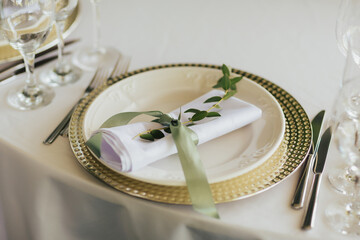 Wedding reception table setting. Napkin wrapped with ribbon and eucalyptus on the plate. Close up.
