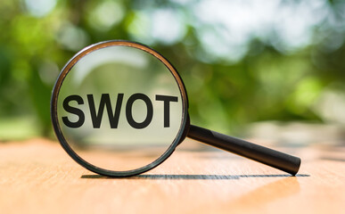 Magnifier glass with text SWOT on blurred nature background.