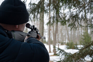 A man with a rifle in the spring forest, the hunter holds a rifle and waits for prey, the hunter...