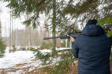 A man with a rifle in the spring forest, the hunter holds a rifle and waits for prey, the hunter...