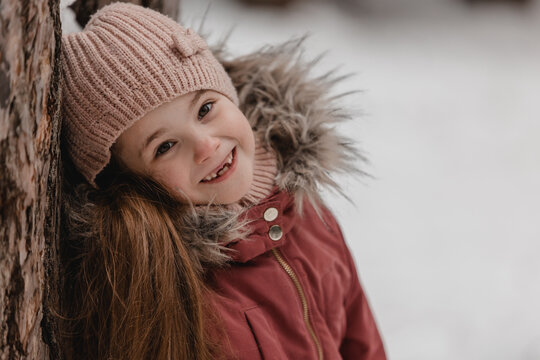 Portrait of little adorable girl in winter hat at snowy forest