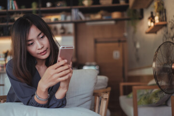 Beautiful Asian business woman holding smart phone and notebook while working in modern cafe with green vertical garden background