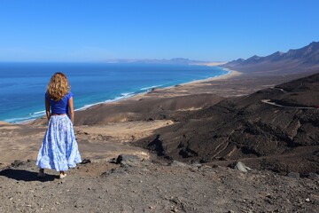 Kobieta w zwiewnej spódnicy podziwiająca widok na ocean oraz dzika plażę Cofete, Fuerteventura