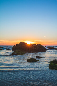Sun is setting behind a rock on the beach in a peaceful scene © Bruno