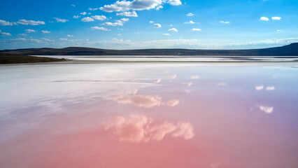 White clouds are reflected in the water surface of a pink lake with salt deposits near the shore. Shooting from a drone.
