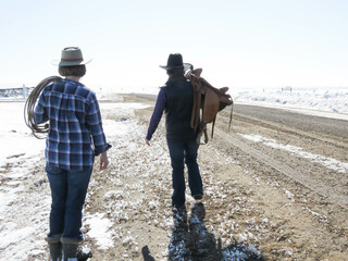 Two people walking down a road in the winter time wit some horse gear.