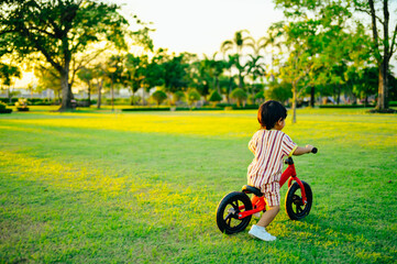 Baby boy riding  balance bike in park with soft-focus and over light in the background