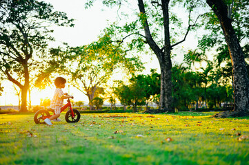 Mother teaches child son to ride a bike,Baby boy riding  balance bike in park with soft-focus and over light on background