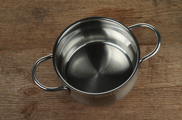 Stainless steel pan without lid on a rough wooden background.