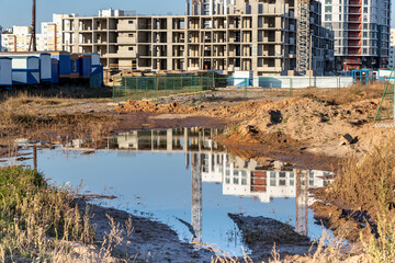 Fototapeta na wymiar A large puddle after rain at the construction site of a large residential facility. Reflection in the water of the construction site and cranes against the background of the sunset sky.