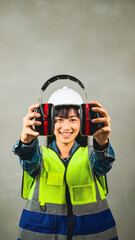 Portrait of a beautiful Asian female engineer is wearing personal protective equipment.Campaign wear hearing protection Ear muffs in construction sites, industry.show personal protective  equipment.